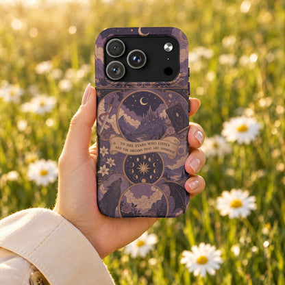 A hand holds a purple fantasy-themed phone case against a blurry background of white daisies.
