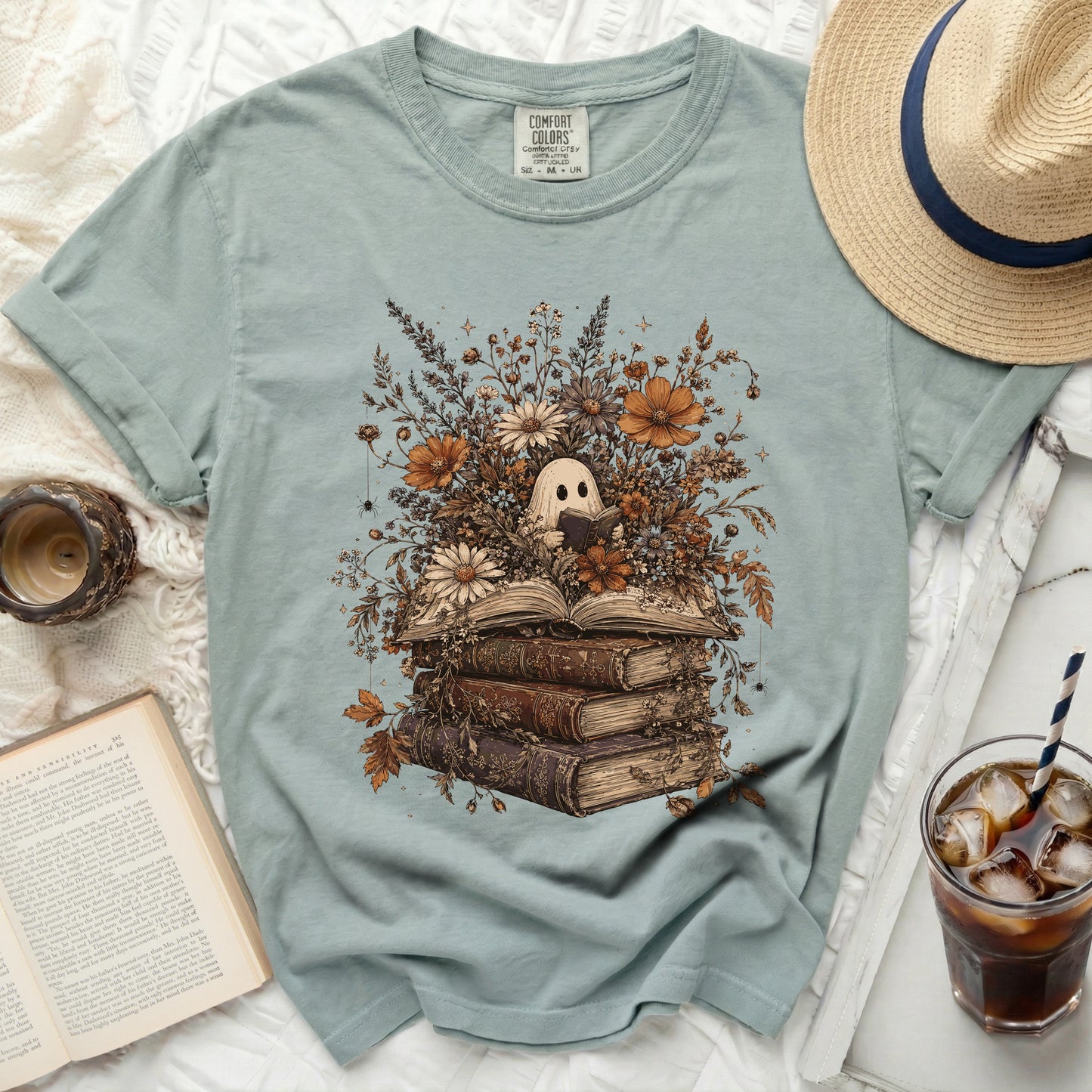 Ghost reading a book surrounded by flowers and old books graphic on a light blue shirt.