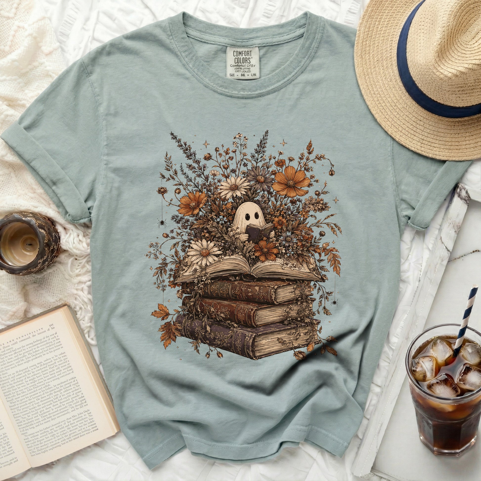 Ghost reading a book surrounded by flowers and old books graphic on a light blue shirt.