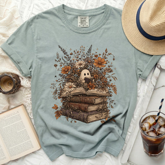 Ghost reading a book surrounded by flowers and old books graphic on a light blue shirt.