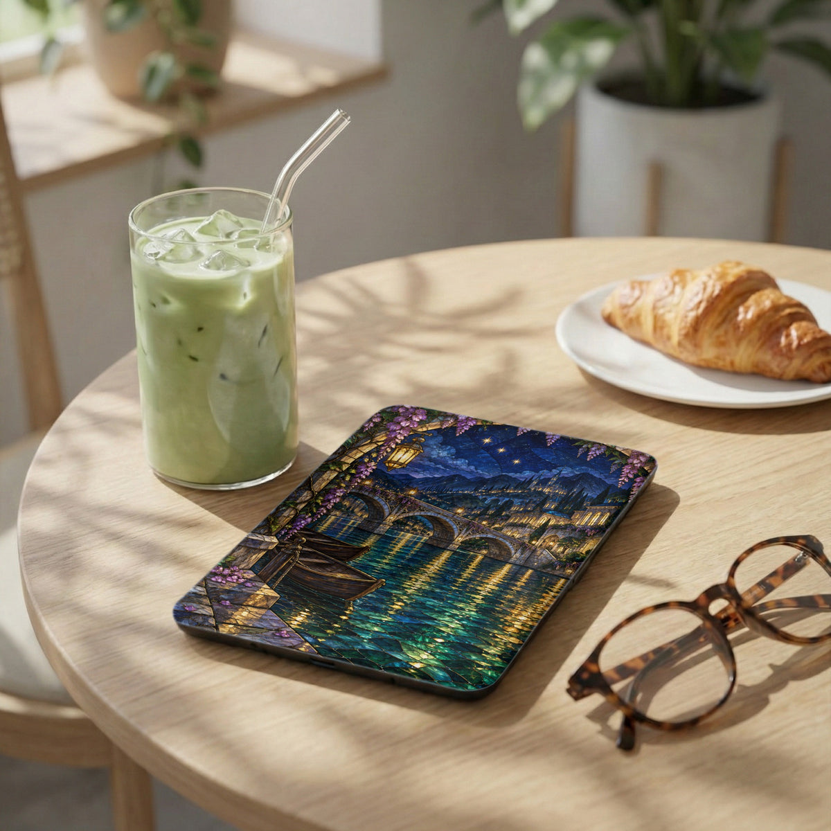 Tablet with a stained glass bridge scene, beside a matcha drink and croissant.