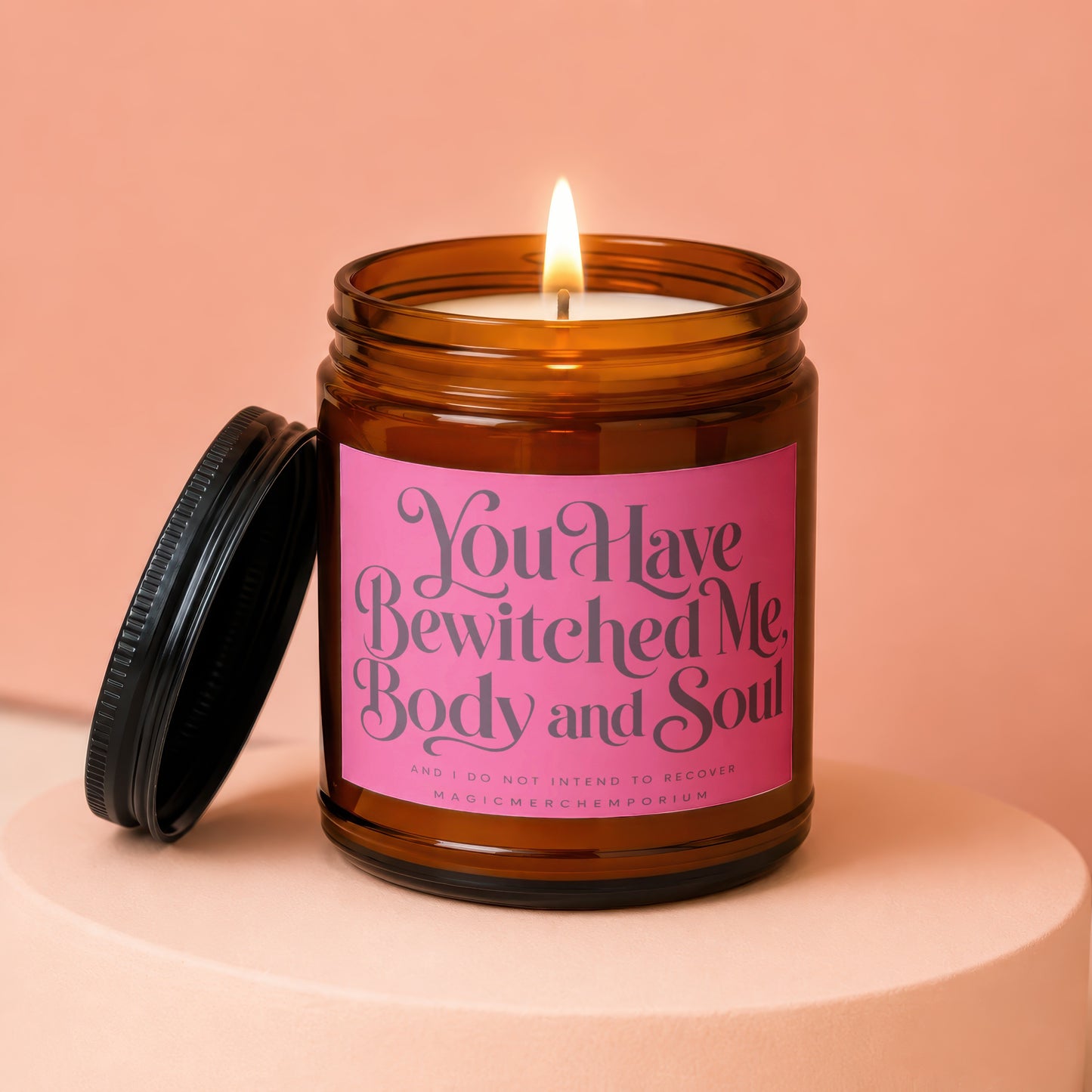 Amber jar candle with lit wick and black lid, reads "You Have Bewitched Me, Body and Soul."