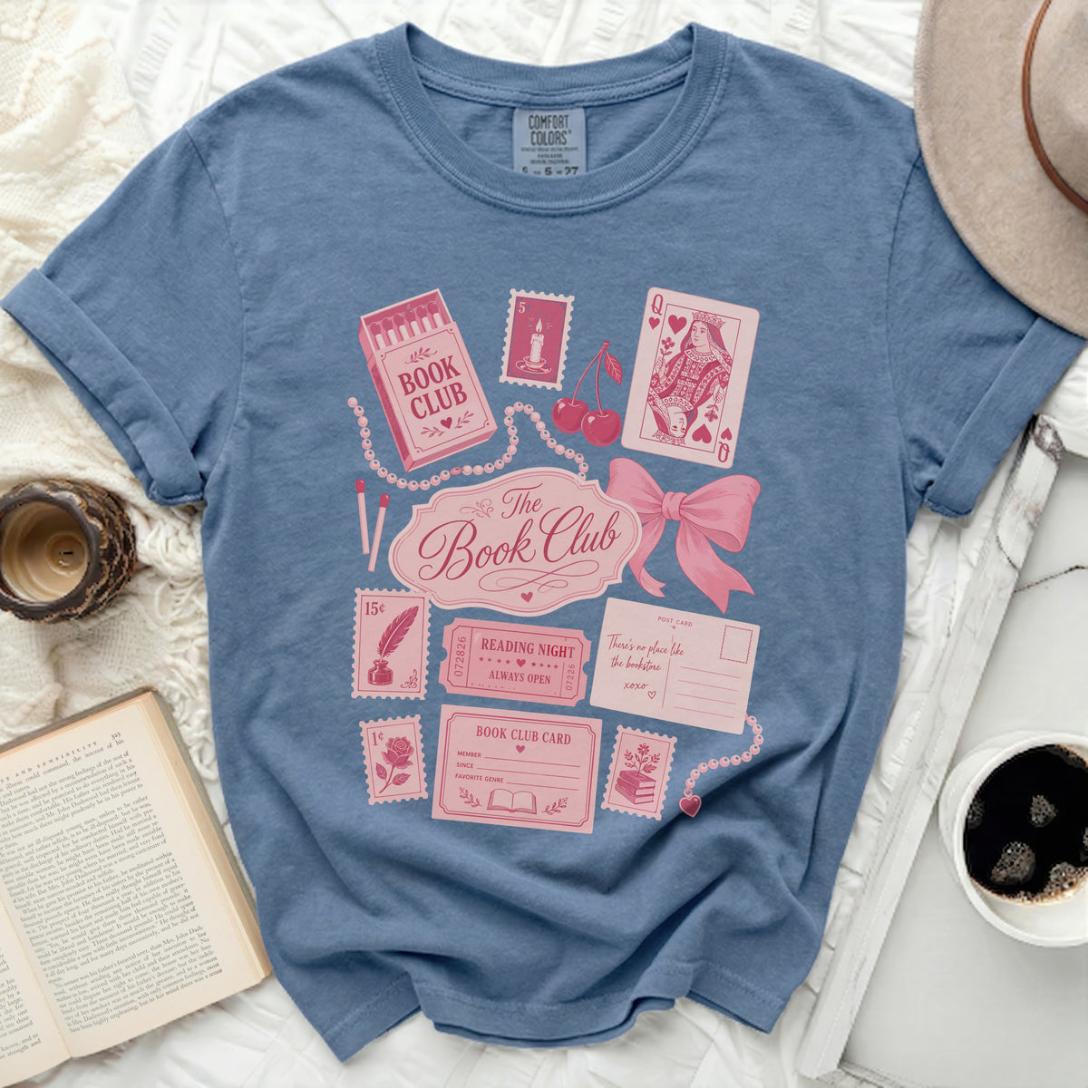 Blue t-shirt with "Book Club" design featuring postage stamps, a postcard, and a bow.