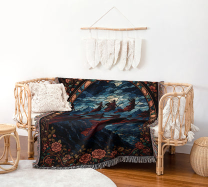 a cozy living room with a wicker bench and a colorful throw blanket on it. The blanket has a vibrant design with a mountain landscape and a boat on the water. Above the bench, there is a wall hanging with white feathers. The room also includes a small table and a woven basket, creating a warm and inviting atmosphere.