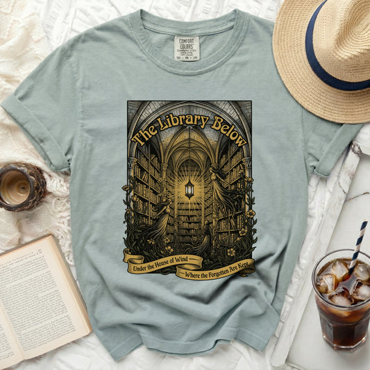 Light blue t-shirt with "The Library Below - Under the House of Wind - Where the Forgotten Are Kept" graphic.
