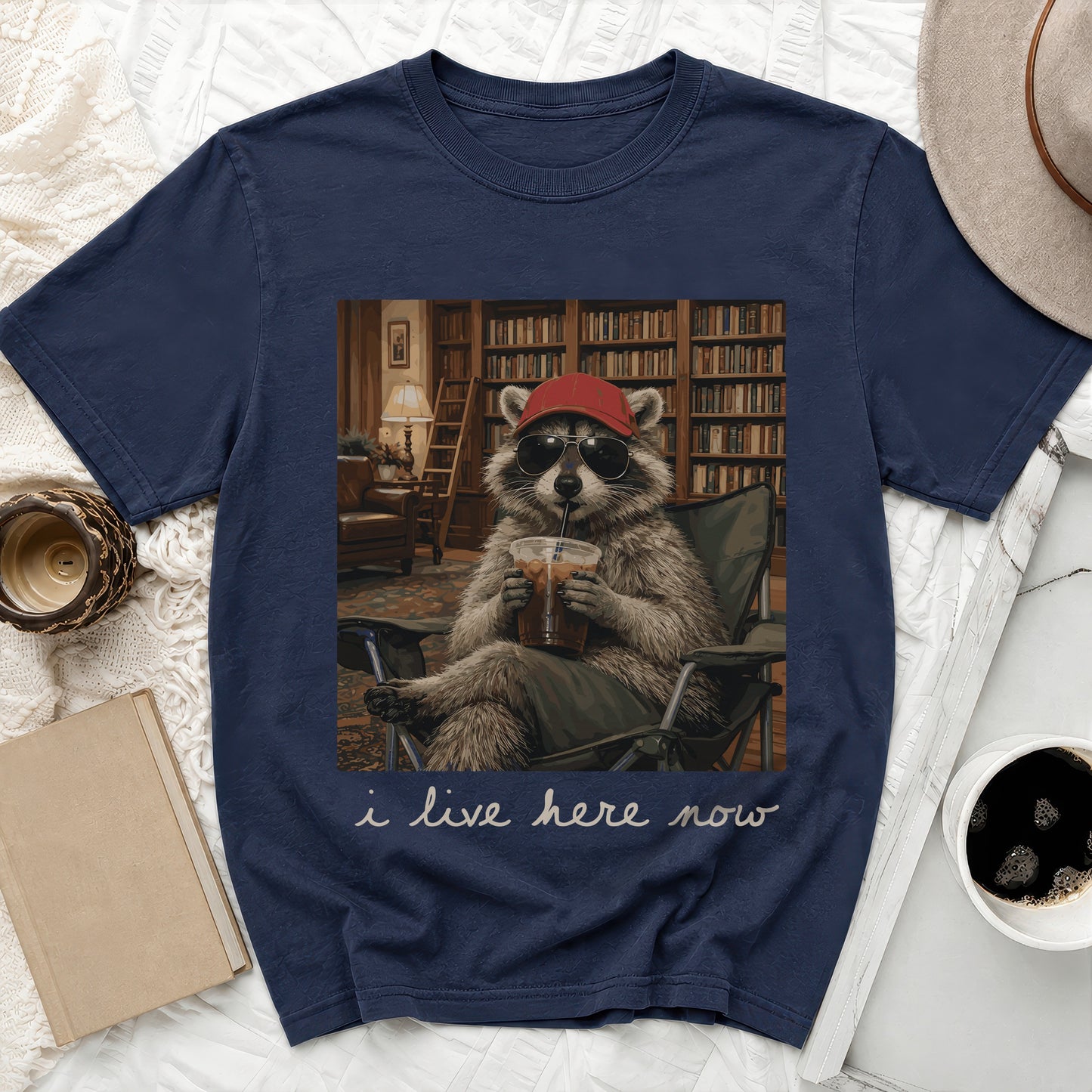 T-shirt graphic of raccoon wearing sunglasses and a red hat, drinking from a cup.