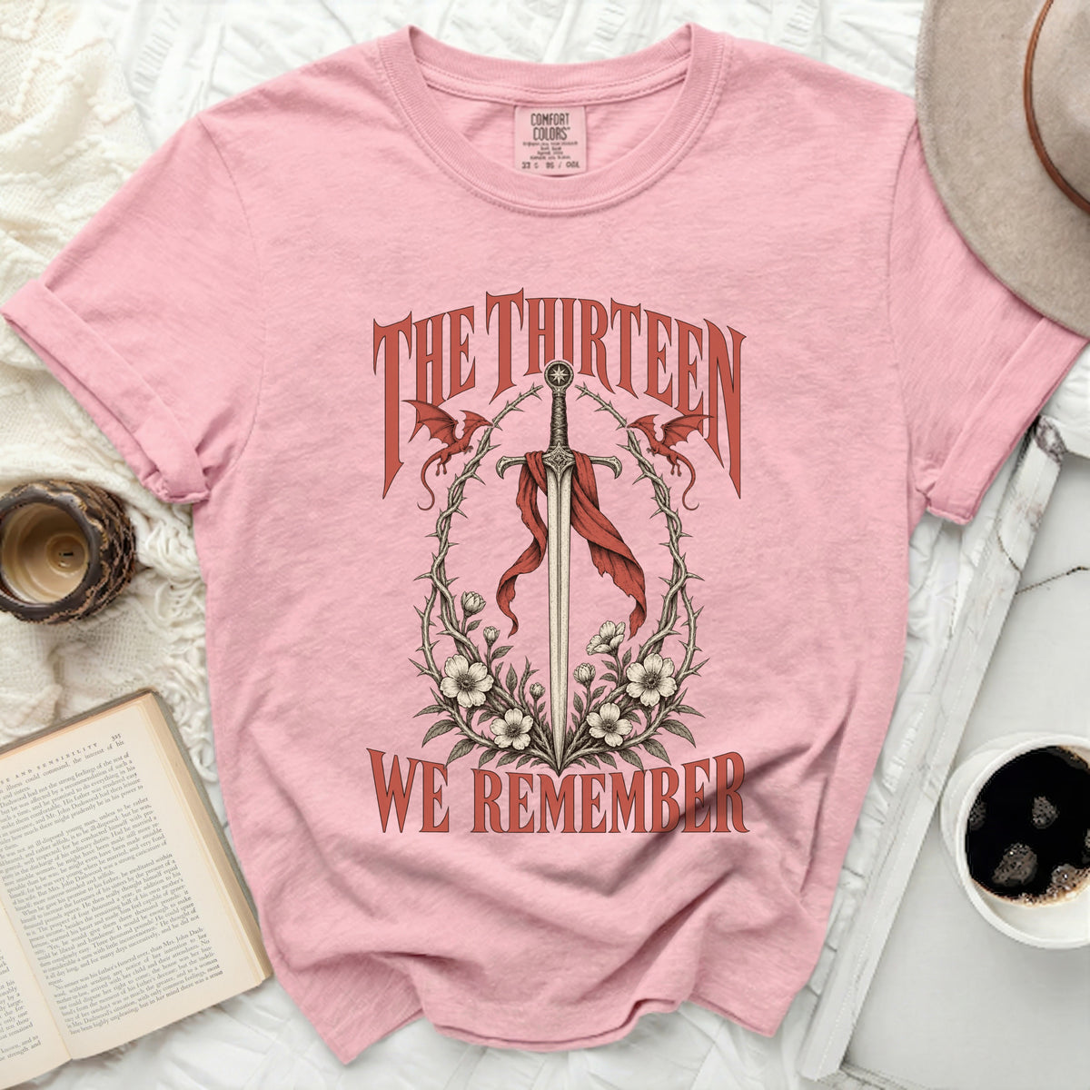 Pink t-shirt with "THE THIRTEEN WE REMEMBER" text and sword graphic.