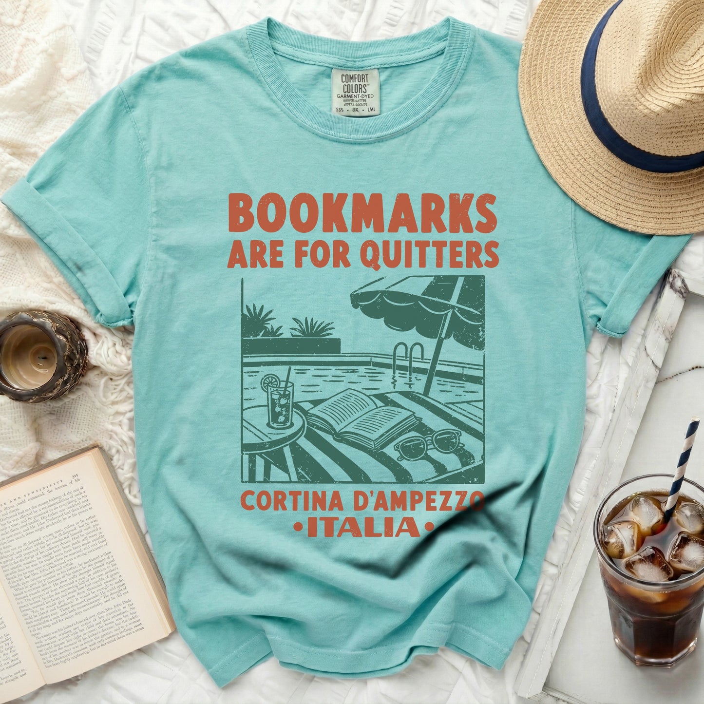 T-shirt with "Bookmarks are for quitters" text, pool scene, and Cortina d'Ampezzo Italia.