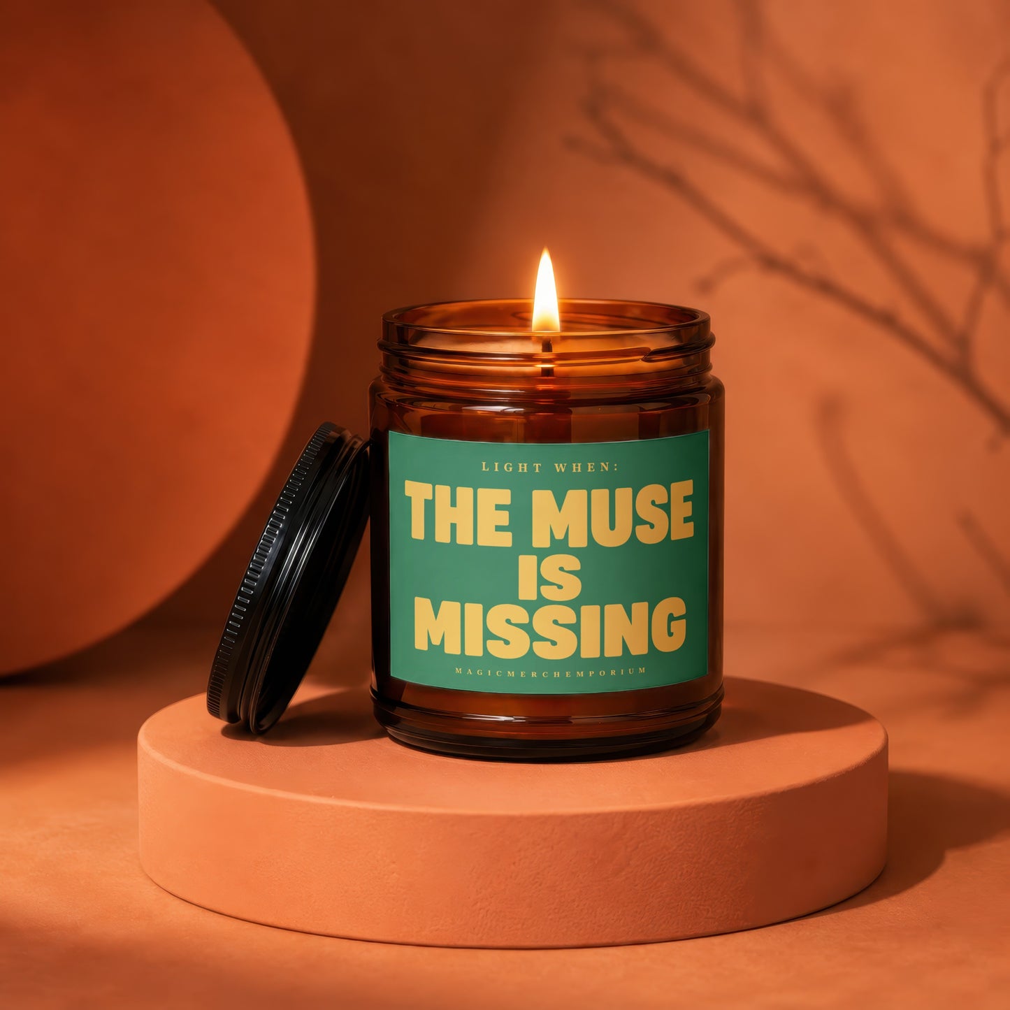 Amber jar candle with lit flame and green label reading "THE MUSE IS MISSING".