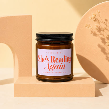 Amber jar candle with "She's Reading Again" text on a light purple label.
