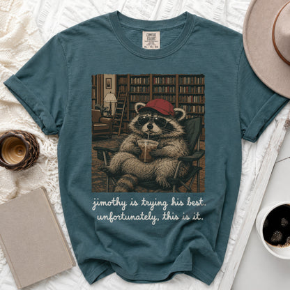 Graphic tee with raccoon in sunglasses and hat holding drink, text "jimothy is trying his best. unfortunately, this is it."