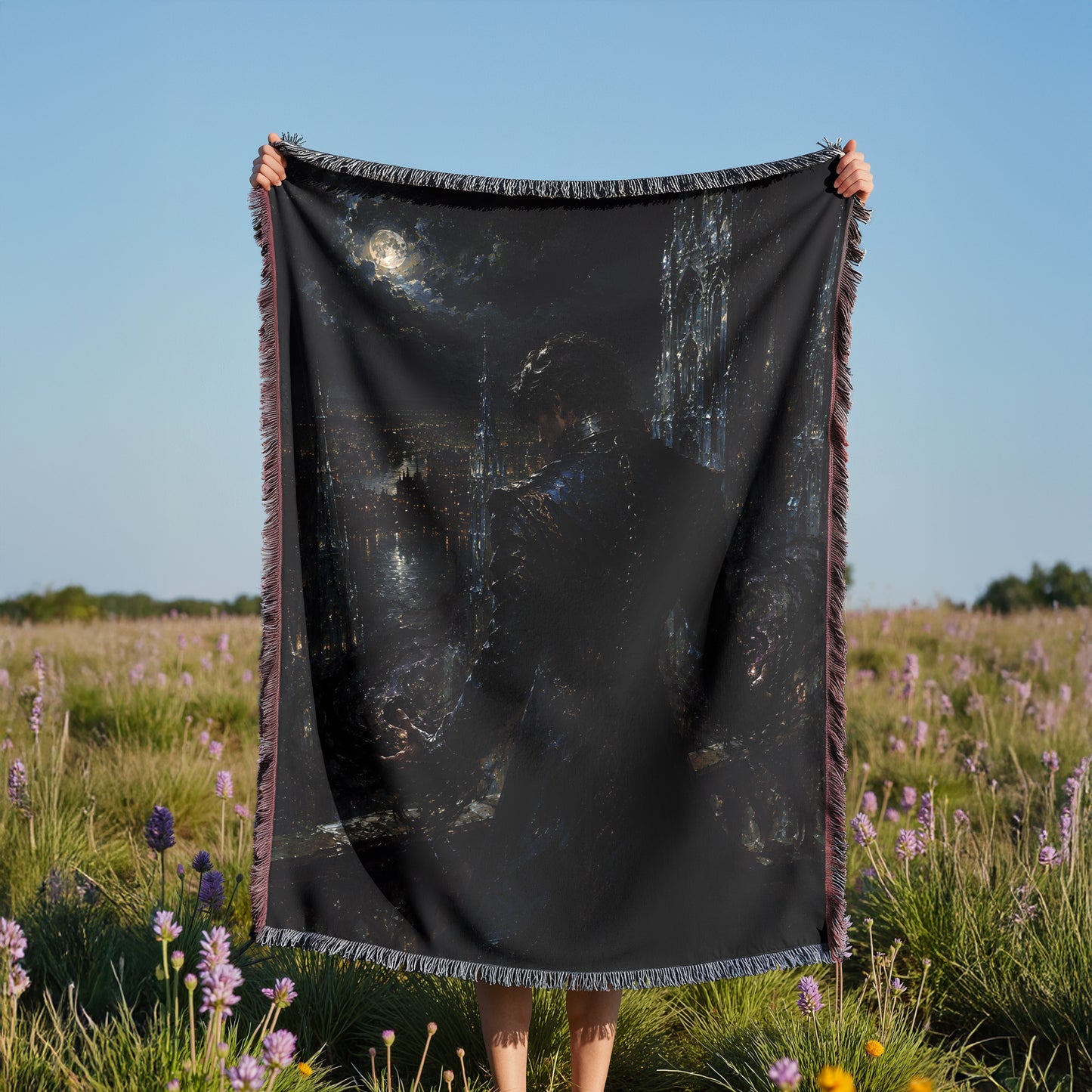 A person is holding up a large black blanket with a painting of a cityscape on it, standing in a field of purple flowers.