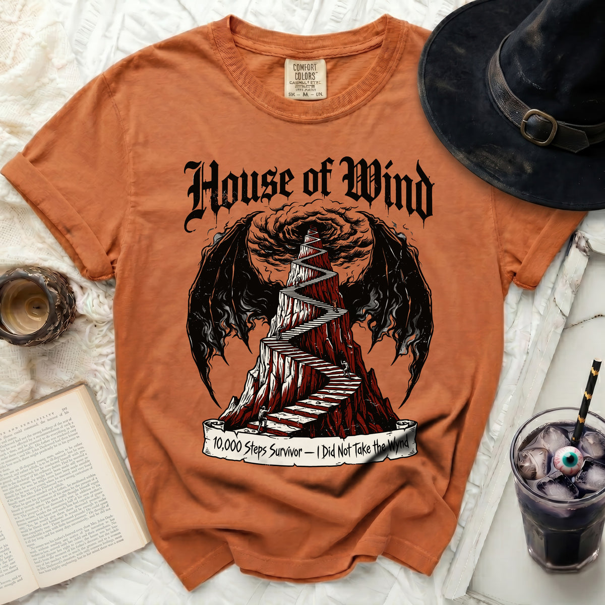 Orange t-shirt with "House of Wind" text and a staircase up a mountain design.