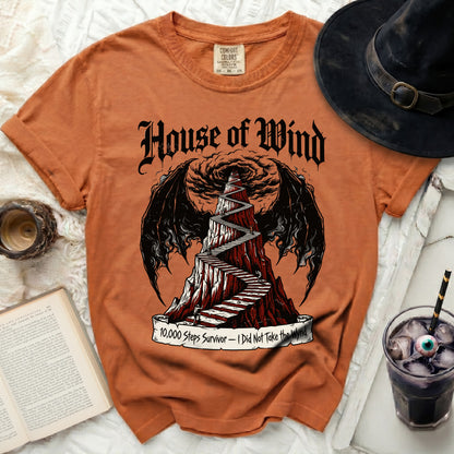 Orange t-shirt with "House of Wind" text and a staircase up a mountain design.