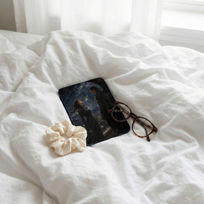 E-reader with fantasy couple cover, glasses, and scrunchie on white sheets