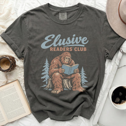 Bigfoot reading a book on a tree stump with "Elusive Readers Club" text.