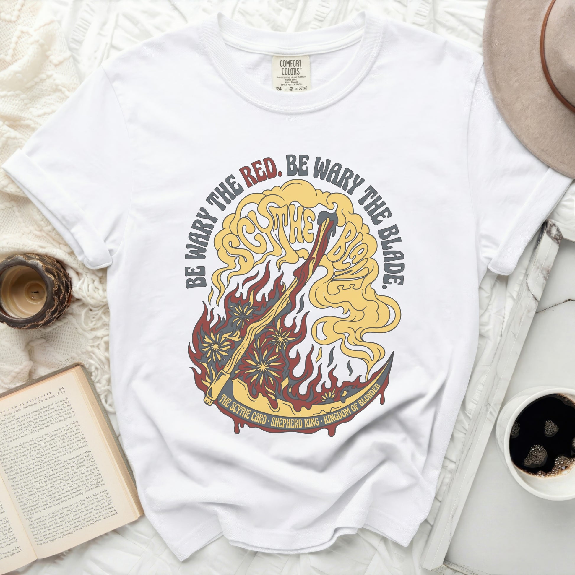 White t-shirt with red, yellow, and gold graphic of a scythe and flames.
