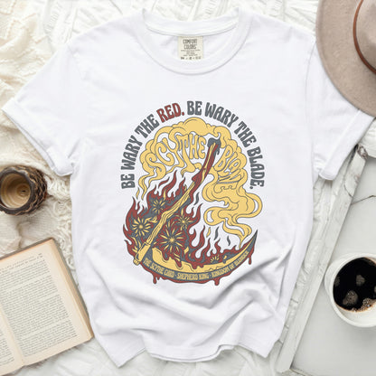 White t-shirt with red, yellow, and gold graphic of a scythe and flames.