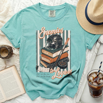 Teal t-shirt with stacked books, hockey helmet, and stick graphic.