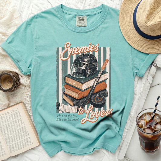 Teal t-shirt with stacked books, hockey helmet, and stick graphic.