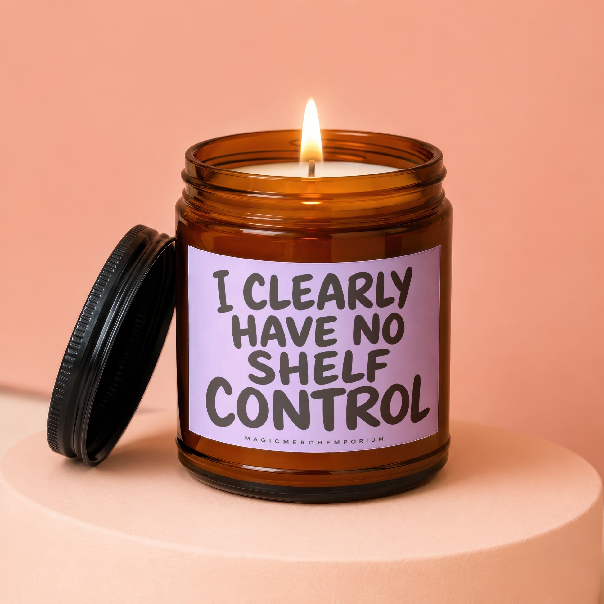 Amber jar candle with a lit wick and a black lid, reads "I CLEARLY HAVE NO SHELF CONTROL".
