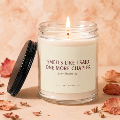A lit candle in a glass jar with a black lid and a label reading "Smells Like I Said One More Chapter."
