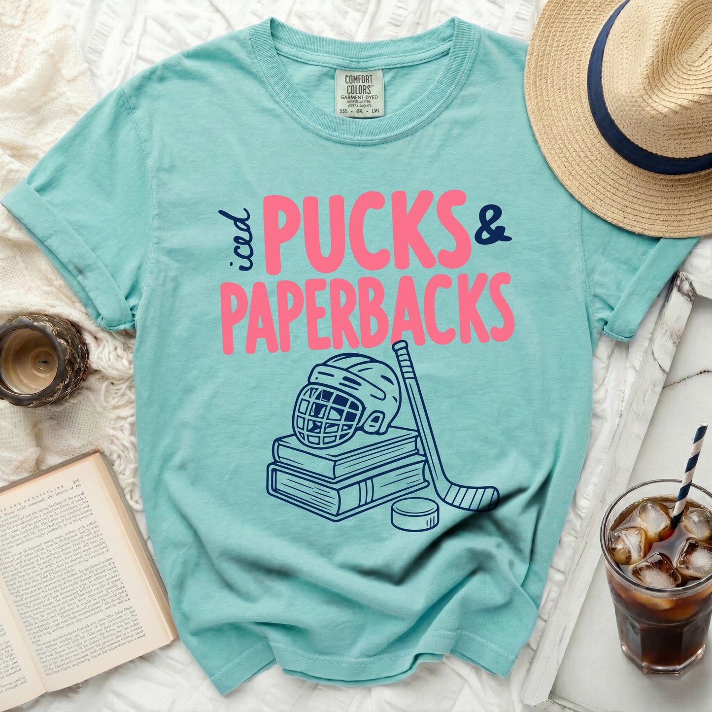 Teal comfort colors t-shirt with pink "Pucks & Paperbacks" and hockey graphics.