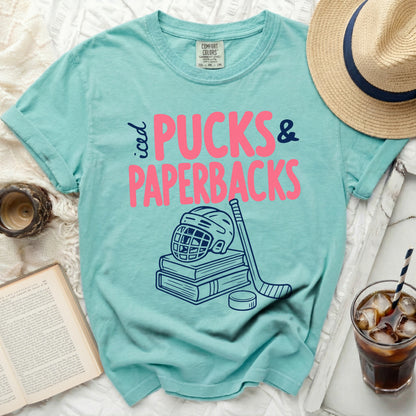 Teal comfort colors t-shirt with pink "Pucks & Paperbacks" and hockey graphics.