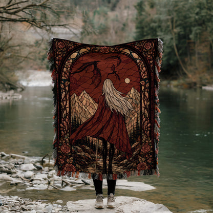 A person stands on a rock, holding a large, ornate blanket with a landscape design, including mountains, trees, and a river.
