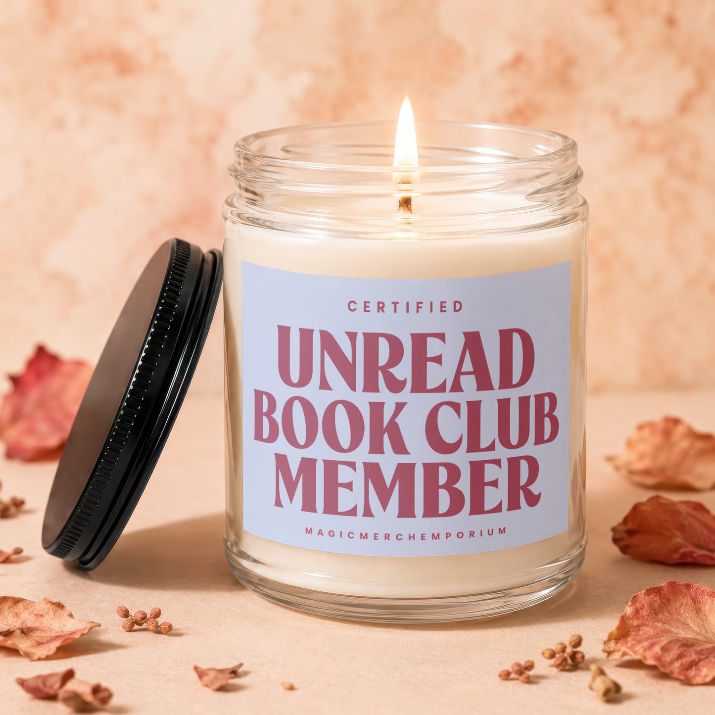 Candle with "Certified Unread Book Club Member" text, lid to the left, fallen leaves.
