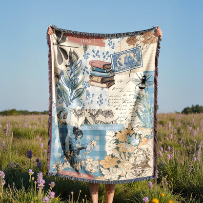 A person is holding up a colorful blanket with various illustrations and text, including a book, flowers, and a bee, in a field with purple flowers.