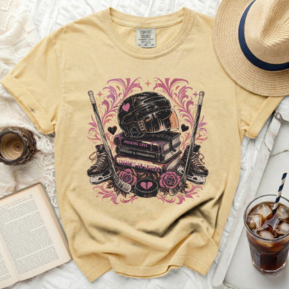 Yellow t-shirt with hockey helmet, skates, pucks, and pink hearts on books.
