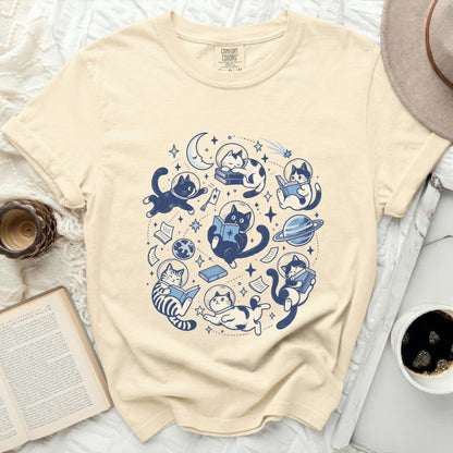 Cream t-shirt with blue astronaut cats reading books and floating in space.