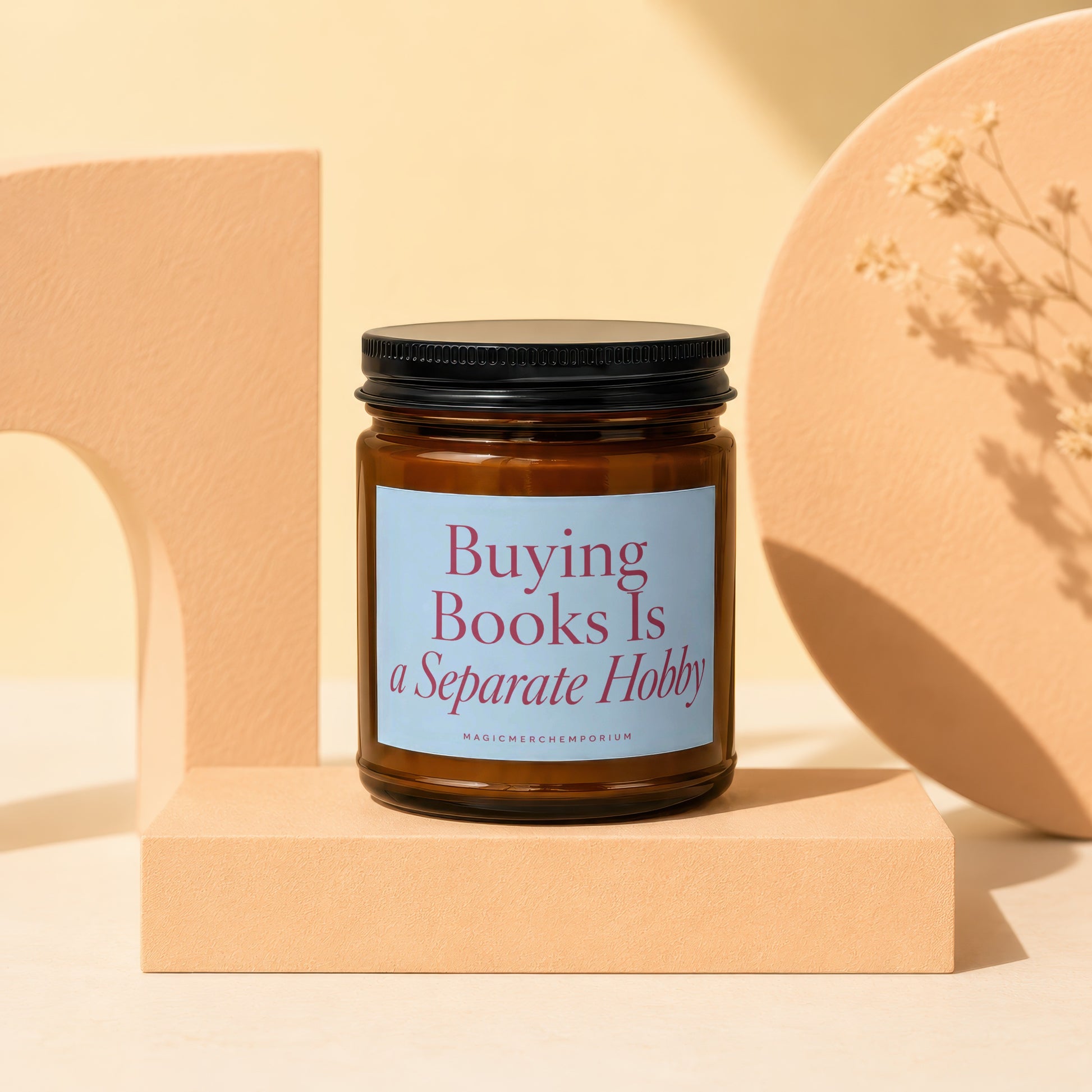 Brown glass candle with black lid, light blue label reading "Buying Books Is a Separate Hobby."