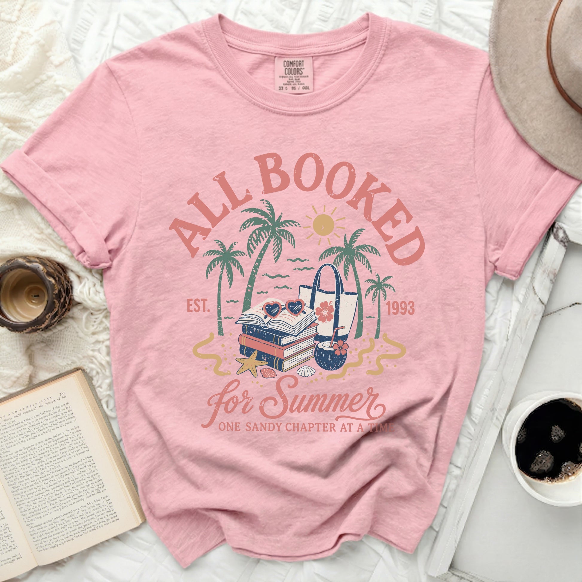 Pink t-shirt with "All Booked for Summer" text and beach imagery.