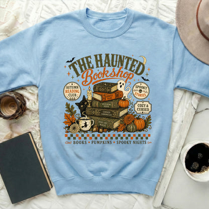 Light blue sweatshirt with "The Haunted Bookshop" graphic featuring books, cat, ghost, and pumpkins.