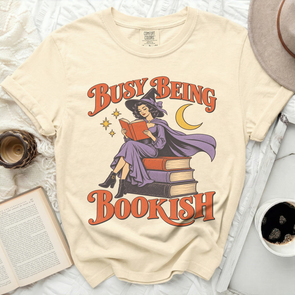 Cream t-shirt with "Busy Being Bookish" text and witch reading on books graphic.