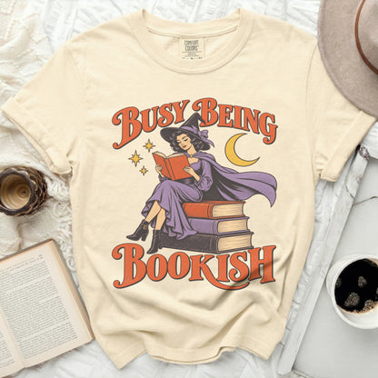 Cream t-shirt with "Busy Being Bookish" text and witch reading on books graphic.