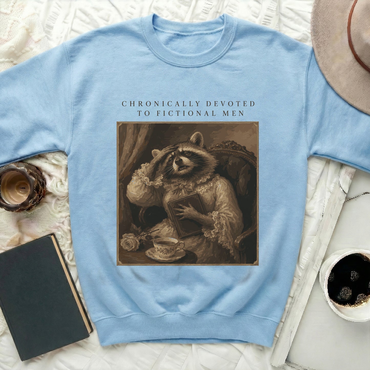 Light blue sweatshirt with a vintage raccoon artwork and text "CHRONICALLY DEVOTED TO FICTIONAL MEN."