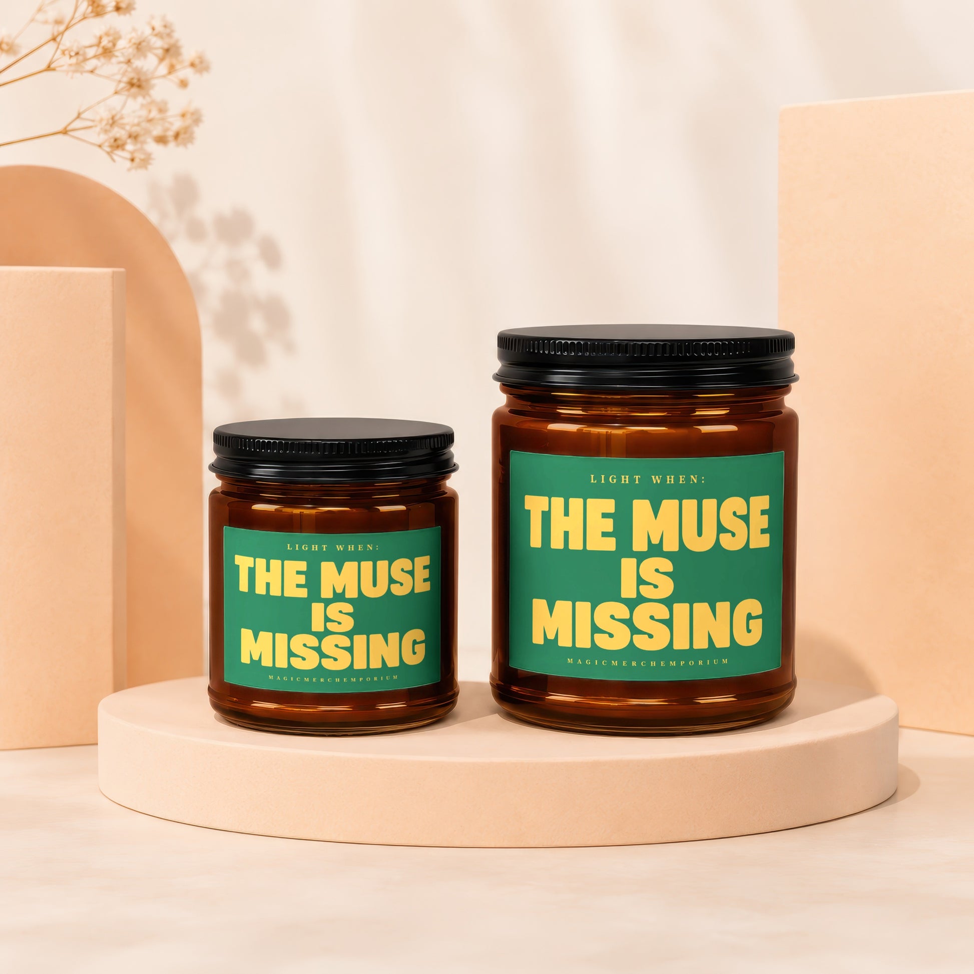 Two amber glass jars with black lids, candles inside, labeled "The Muse Is Missing".