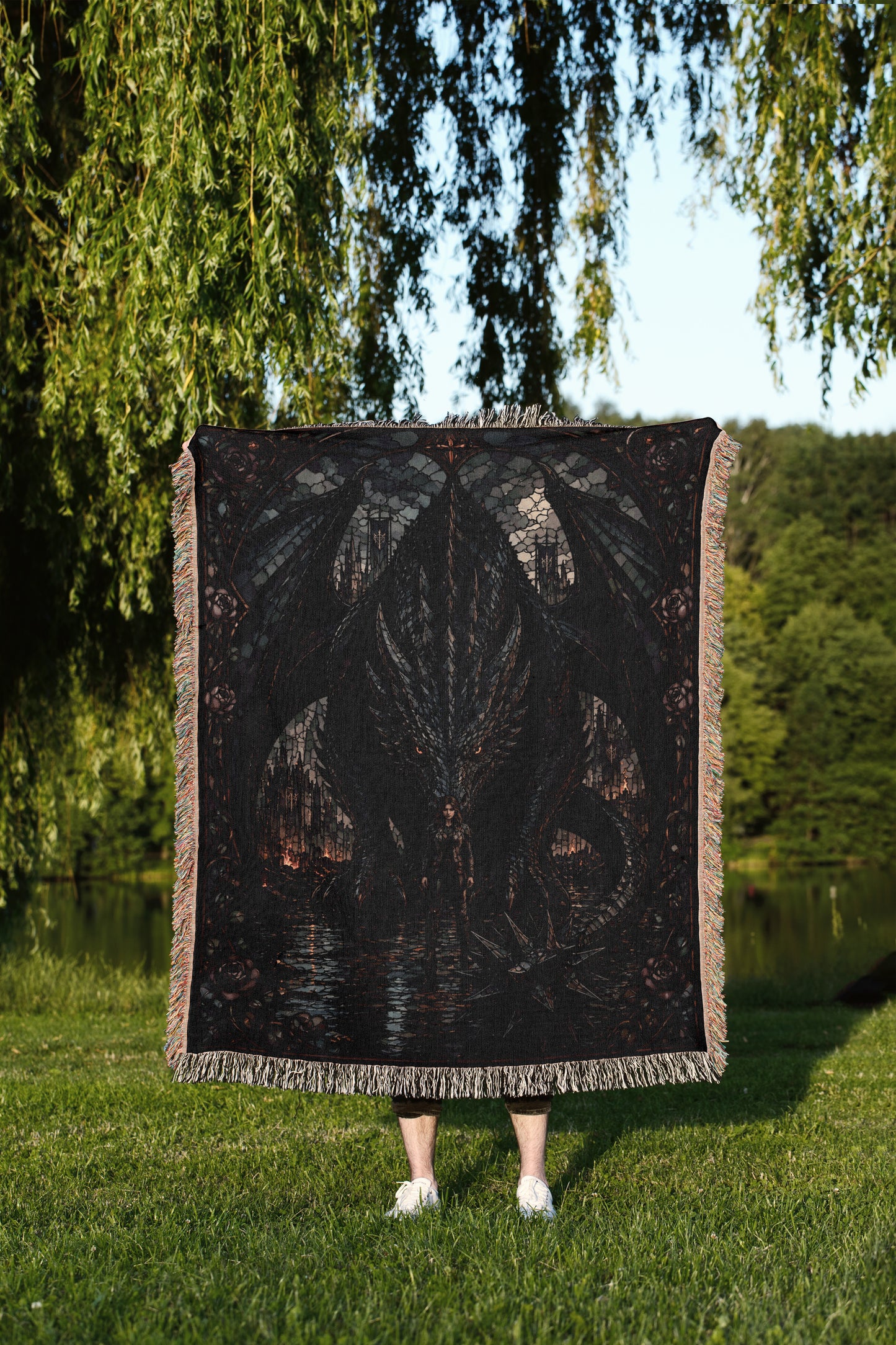 A person standing in a grassy field, partially obscured by a large, dark-colored blanket featuring a dragon design.