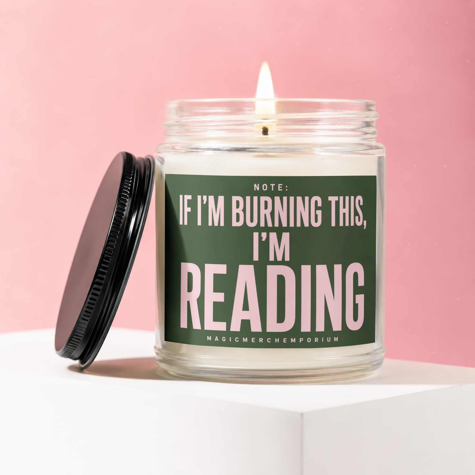 Glass candle with lit wick and black lid, reads "NOTE: IF I'M BURNING THIS, I'M READING".