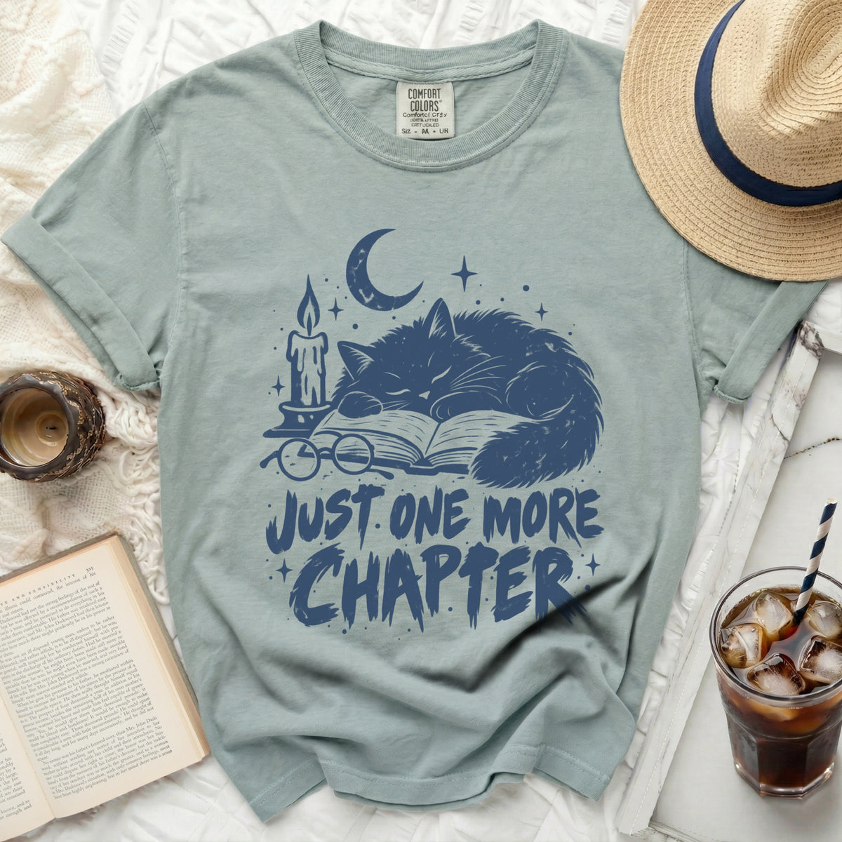 T-shirt with dark blue graphic of sleeping cat, book, candle, and text "JUST ONE MORE CHAPTER".