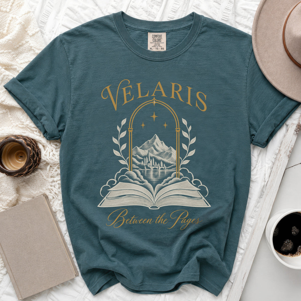 Teal t-shirt with gold text "Velaris Between the Pages" and a landscape illustration.