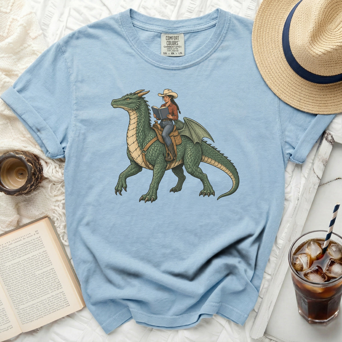 Light blue t-shirt with graphic of cowgirl riding and reading on a green dragon.