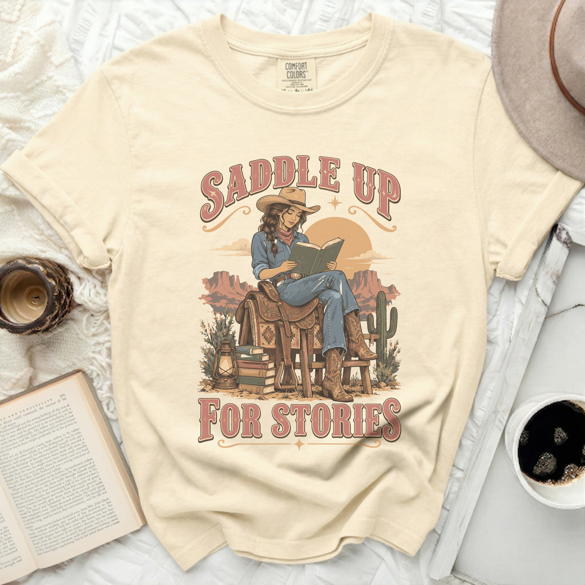 Graphic tee with "Saddle Up For Stories" text and a cowgirl reading a book.