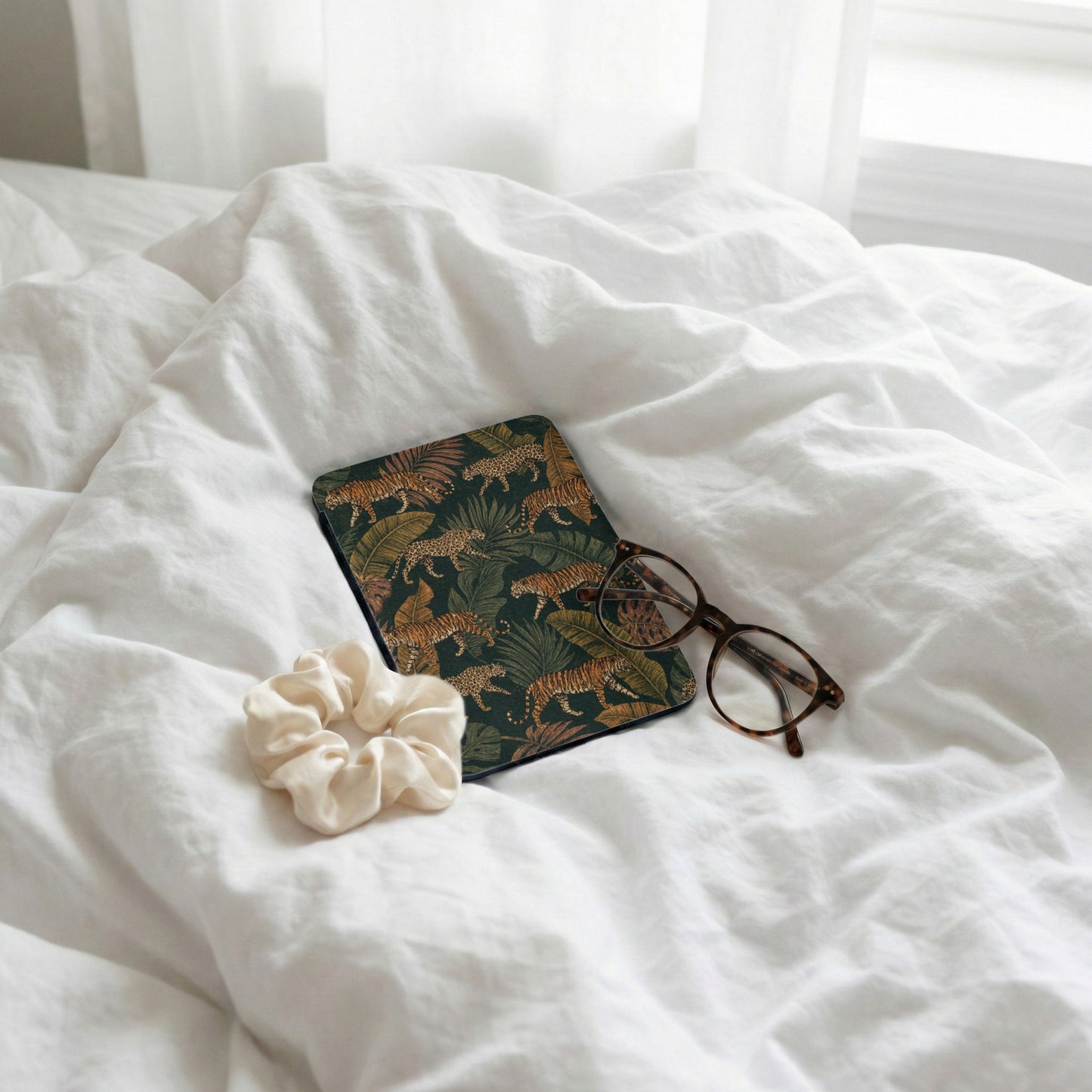 Journal with tiger print and glasses on wrinkled white sheets.