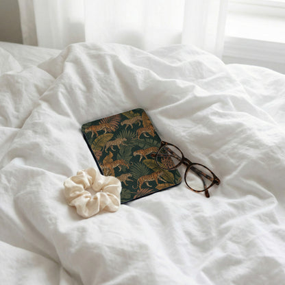 Journal with tiger print and glasses on wrinkled white sheets.