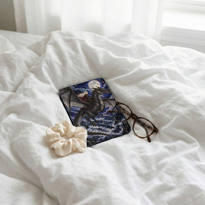 Book with dragon and rider artwork, scrunchie, and glasses on white bedding.