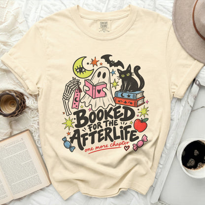 Cream t-shirt with ghost, skeleton, black cat, and books graphic. Text reads "Booked for the Afterlife, one more chapter."